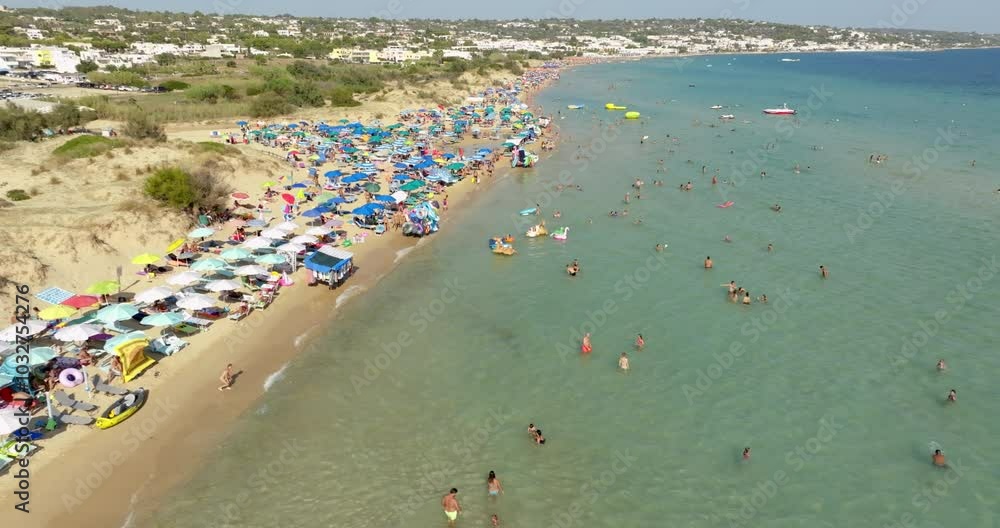 Aerial view of Pescoluse beach in Salento, Puglia, Italy. This beach is also called the Maldives of Salento. There are many umbrellas on the beach and tourists at the sea. Aerial view of Pescoluse beach in Salento, Puglia, Italy. This beach is also called the Maldives of Salento. There are many umbrellas on the beach and tourists at the sea.