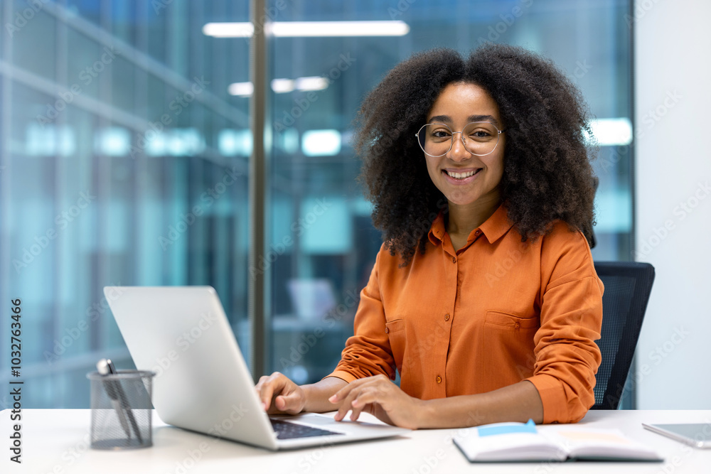 Smiling young professional woman working on a laptop at a modern office desk, exuding confidence and focus Smiling young professional woman working on a laptop at a modern office desk, exuding confidence and focus