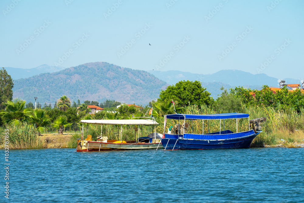 Pleasure boats at pier on Dalyan River, Turkey on a sunny clear summer day. Concept of water travel and the Mediterranean climate. River or water landscape Pleasure boats at pier on Dalyan River, Turkey on a sunny clear summer day. Concept of water travel and the Mediterranean climate. River or water landscape