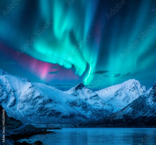 Aurora borealis over the snowy mountains, frozen sea, reflection in water at winter night in Lofoten, Norway. Northern lights  and snowy rocks. Landscape with polar lights, road, starry sky and fjord photo