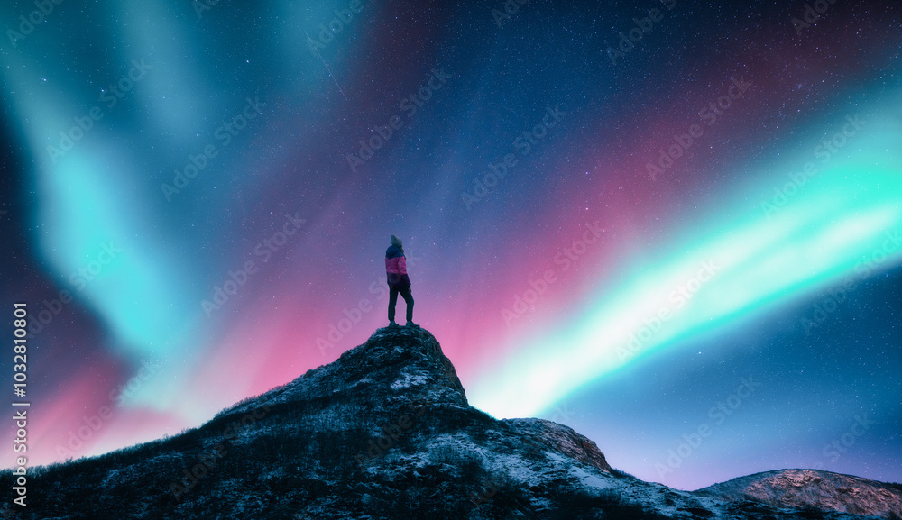 Aurora borealis and sporty woman on mountain peak at night. Northern lights and silhouette of a girl on top of rock. Lofoten islands, Norway. Landscape with polar lights. Starry sky with bright aurora Aurora borealis and sporty woman on mountain peak at night. Northern lights and silhouette of a girl on top of rock. Lofoten islands, Norway. Landscape with polar lights. Starry sky with bright aurora