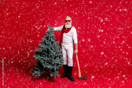 Full length photo of cheerful retired man holding fir tree having eyeglasses eyewear wearing boots white pullover pants isolated over red background photo