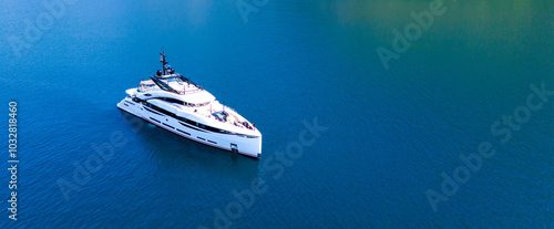 A snow-white modern yacht stands at anchor in an azure bay