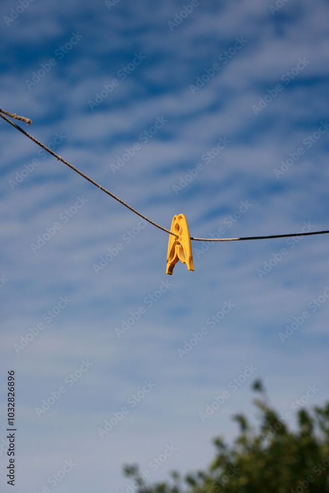 A Single Yellow Clothespin Is Clipped To A Clothesline, Standing Out Against A Clear Blue Sky. The Image Conveys Simplicity And Tranquility, With A Touch Of Everyday Life...