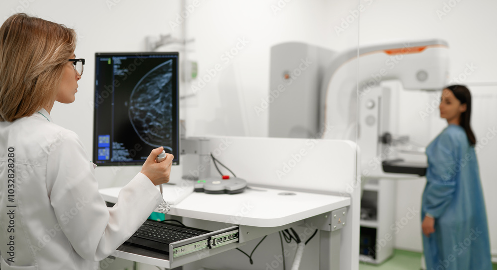Female doctor examines breast scan on monitor while patient in blue gown undergoes mammogram screening in the background, showcasing advanced breast cancer detection technology in medical facility. Female doctor examines breast scan on monitor while patient in blue gown undergoes mammogram screening in the background, showcasing advanced breast cancer detection technology in medical facility.
