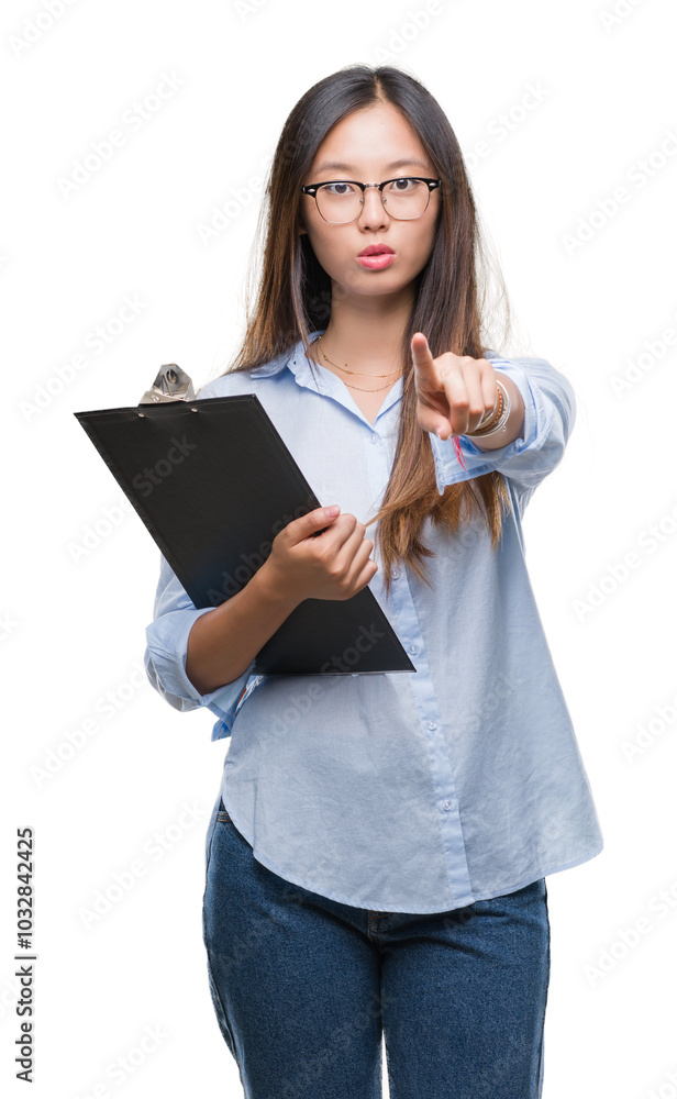 Young asian business woman holding clipboard over isolated background pointing with finger to the camera and to you, hand sign, positive and confident gesture from the front Young asian business woman holding clipboard over isolated background pointing with finger to the camera and to you, hand sign, positive and confident gesture from the front