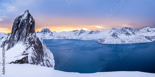Panorama of Segla mountain peak and Fjord seen from Hesten trail near Fjordgard on Senja island, Norway in winter. Scenic winter landscape with snowy mountains range and cold fjord water at sunset