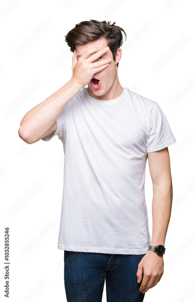 Young handsome man wearing casual white t-shirt over isolated background peeking in shock covering face and eyes with hand, looking through fingers with embarrassed expression. Young handsome man wearing casual white t-shirt over isolated background peeking in shock covering face and eyes with hand, looking through fingers with embarrassed expression.
