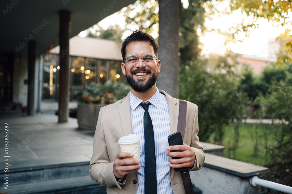 © Zamrznuti tonovi - Happy businessman holding coffee and smartphone walking in the city © Zamrznuti tonovi - Happy businessman holding coffee and smartphone walking in the city
