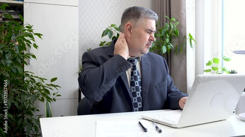 A man working at a computer has a sore neck. He rubs his neck to relieve the pain. Suitable for content about freelancing and remote work.