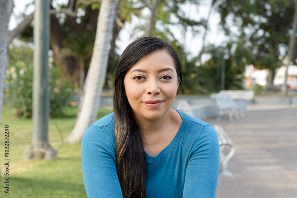 Young woman smiling and looking at the camera, in a park with green grass and trees blurred in the background. Young woman smiling and looking at the camera, in a park with green grass and trees blurred in the background.