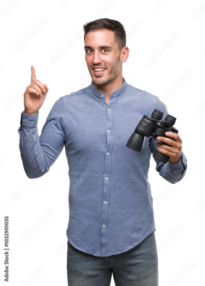 Handsome young man looking through binoculars surprised with an idea or question pointing finger with happy face, number one Handsome young man looking through binoculars surprised with an idea or question pointing finger with happy face, number one