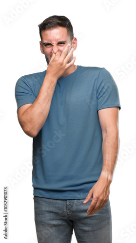 Handsome young casual man smelling something stinky and disgusting, intolerable smell, holding breath with fingers on nose. Bad smells concept.