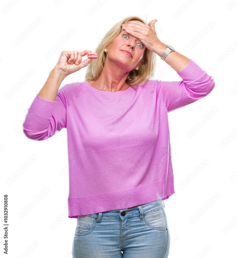Middle age blonde woman eatin pink macaron biscuit over isolated background stressed with hand on head, shocked with shame and surprise face, angry and frustrated. Fear and upset for mistake. Middle age blonde woman eatin pink macaron biscuit over isolated background stressed with hand on head, shocked with shame and surprise face, angry and frustrated. Fear and upset for mistake.