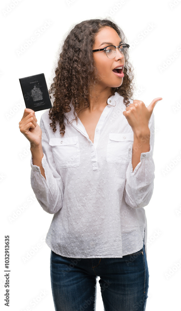 Young hispanic woman holding passport of Canada pointing and showing with thumb up to the side with happy face smiling Young hispanic woman holding passport of Canada pointing and showing with thumb up to the side with happy face smiling