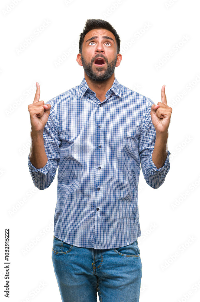 Adult hispanic man over isolated background amazed and surprised looking up and pointing with fingers and raised arms. Adult hispanic man over isolated background amazed and surprised looking up and pointing with fingers and raised arms.