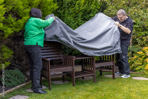 фотографія Senior couple put garden seat cover onto outdoor furniture bench set in home bac