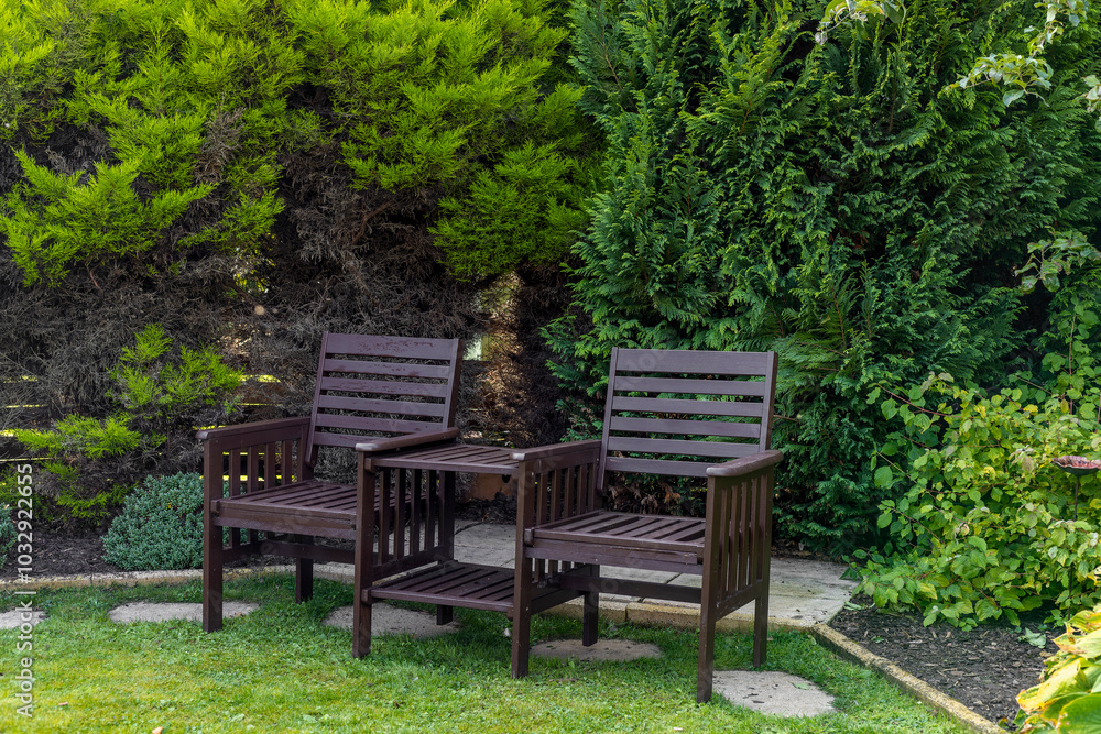 Two seat wooden garden bench set with table top on grass lawn in lush green garden Two seat wooden garden bench set with table top on grass lawn in lush green garden