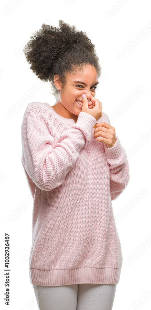Young afro american woman wearing winter sweater over isolated background smelling something stinky and disgusting, intolerable smell, holding breath with fingers on nose. Bad smells concept. Young afro american woman wearing winter sweater over isolated background smelling something stinky and disgusting, intolerable smell, holding breath with fingers on nose. Bad smells concept.