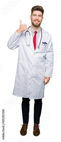 Young handsome doctor man wearing medical coat smiling doing phone gesture with hand and fingers like talking on the telephone. Communicating concepts.