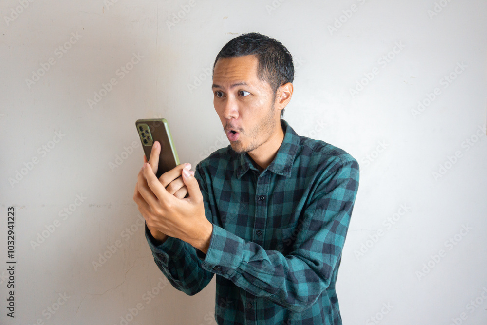 Young men wearing green flannel is shock by his smartphone on isolated white background Young men wearing green flannel is shock by his smartphone on isolated white background