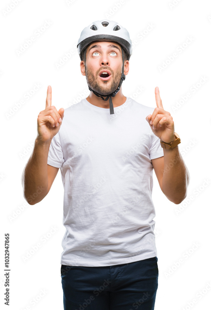 Young handsome man wearing cyclist safety helmet over isolated background amazed and surprised looking up and pointing with fingers and raised arms. Young handsome man wearing cyclist safety helmet over isolated background amazed and surprised looking up and pointing with fingers and raised arms.