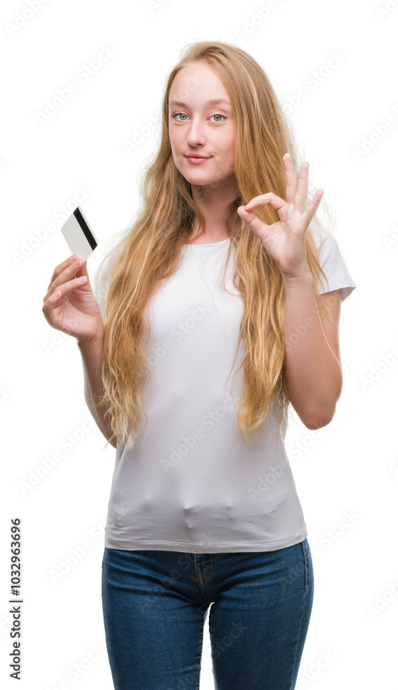 Obraz premium Blonde teenager woman holding credit card doing ok sign with fingers, excellent symbol