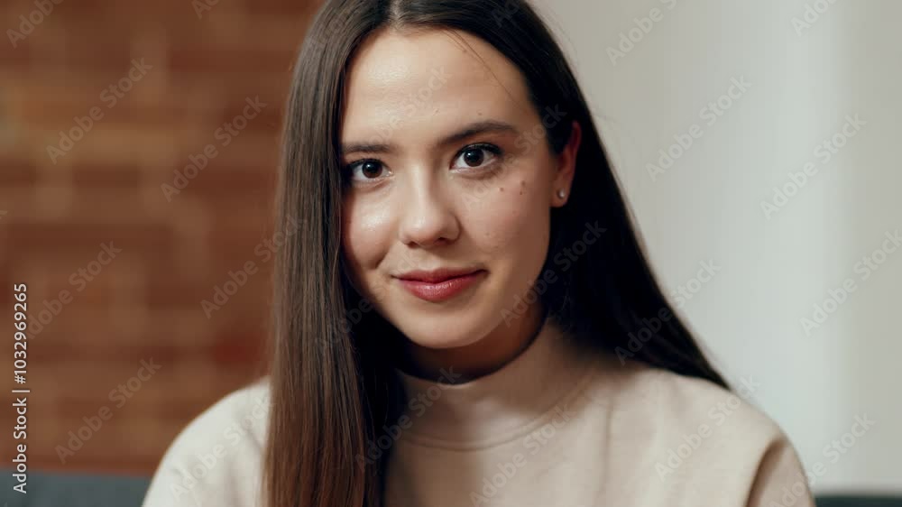 A young woman with long hair sits comfortably indoors, wearing a soft sweater. She smiles warmly, exuding confidence in a well-lit, cozy environment with brick walls. A young woman with long hair sits comfortably indoors, wearing a soft sweater. She smiles warmly, exuding confidence in a well-lit, cozy environment with brick walls.
