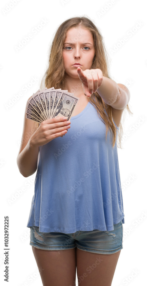 Young blonde woman holding dollars pointing with finger to the camera and to you, hand sign, positive and confident gesture from the front Young blonde woman holding dollars pointing with finger to the camera and to you, hand sign, positive and confident gesture from the front