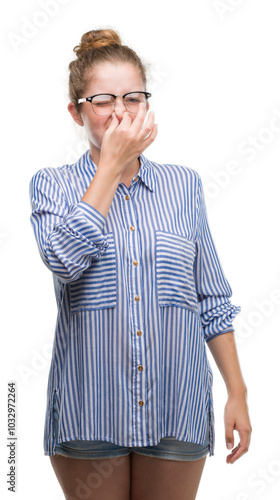 Young blonde business woman smelling something stinky and disgusting, intolerable smell, holding breath with fingers on nose. Bad smells concept. photo