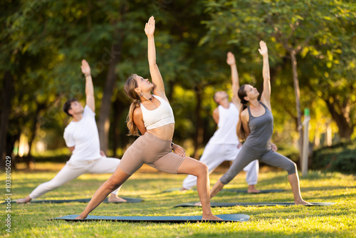 People group in park practicing yoga outdoor. Active pastime together, performing gymnastic exercise. Yoga lesson visitors perform warrior pose. People practice sports during yoga in nature photo