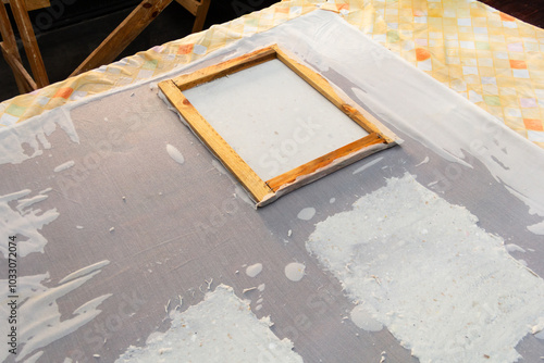 A deckle mold and recycled paper sheets laying over a workshop table drying to create recycled paper sheets from reusable material. photo