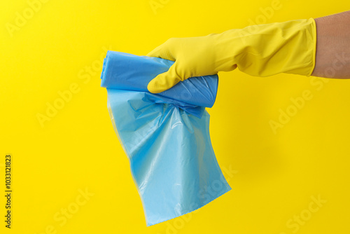 Roll of garbage bags in gloved hand on yellow background