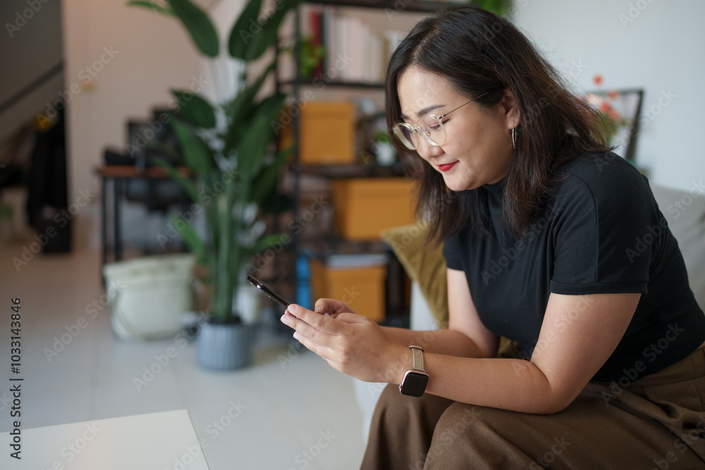 Asian woman sits on sofa using smartphone checking social media, chatting, searching information Asian woman sits on sofa using smartphone checking social media, chatting, searching information