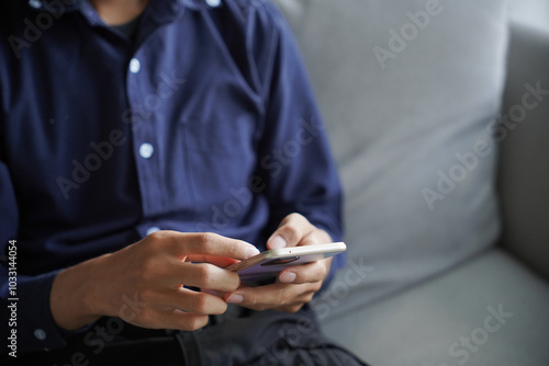 Man using smartphone chatting, checking social media by touch screen, He sitting on sofa in living room at home