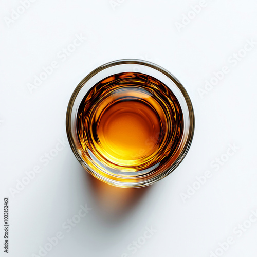 A glass filled with amber liquid, likely a spirit or whiskey, on a white surface.