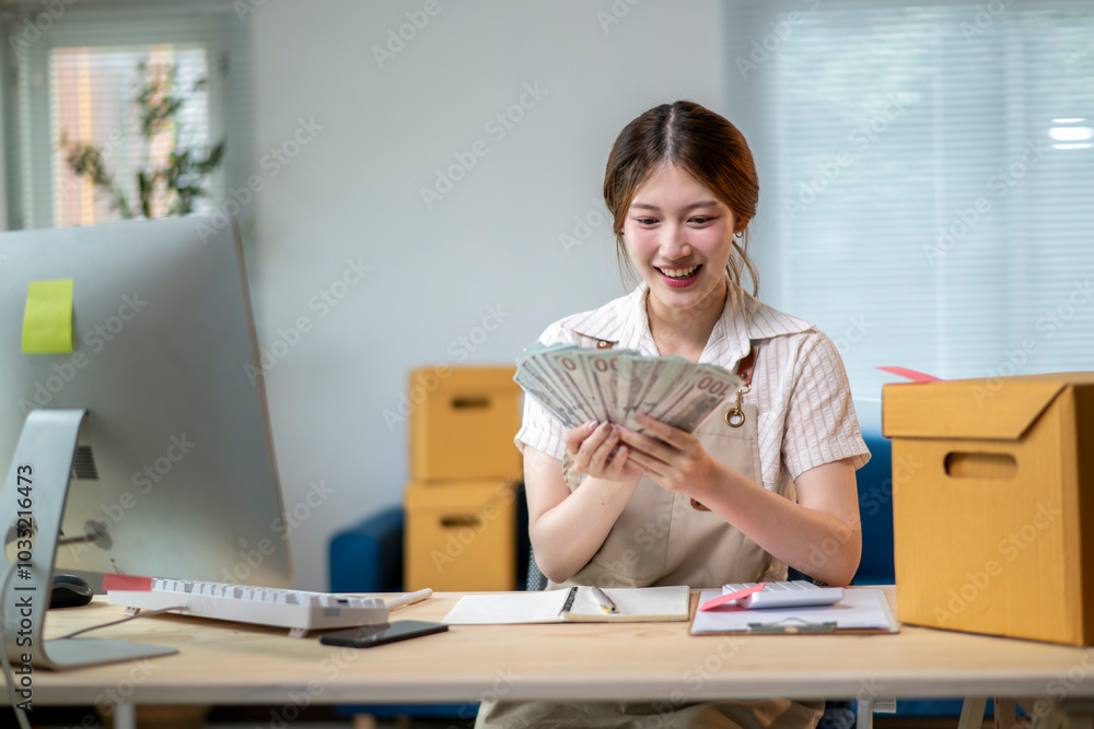 A woman is sitting at a desk with a computer and a stack of money A woman is sitting at a desk with a computer and a stack of money