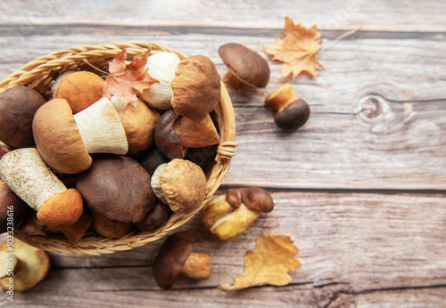A woven basket filled with various mushrooms and autumn leaves on a wooden surface in a cozy kitchen setting