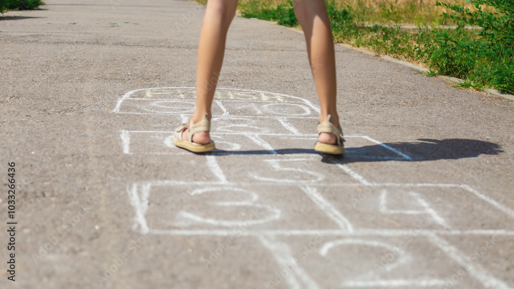 Closeup of little girl's legs and hopscotch drawn on asphalt. Child playing hopscotch game on outdoors on a sunny day. Summer activities for children. Closeup of little girl's legs and hopscotch drawn on asphalt. Child playing hopscotch game on outdoors on a sunny day. Summer activities for children.