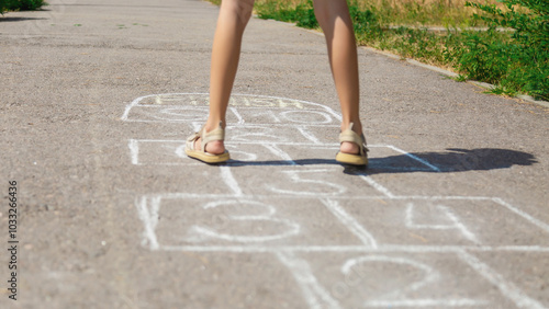 Closeup of little girl's legs and hopscotch drawn on asphalt. Child playing hopscotch game on outdoors on a sunny day. Summer activities for children.