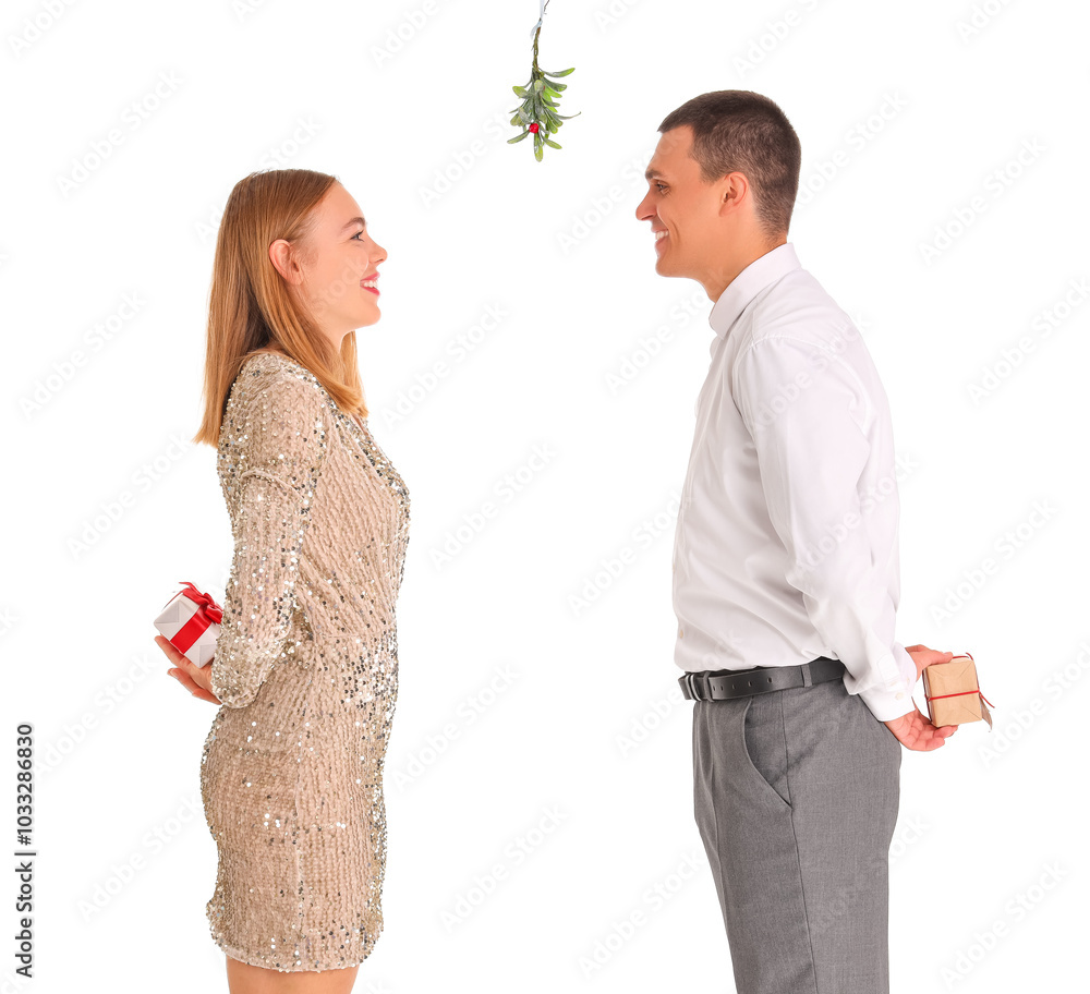 Young couple with Christmas gifts and mistletoe branch on white background