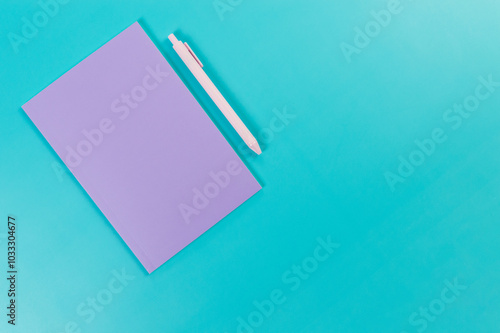 Top view of purple notebook, pink pen on blue background. School, office wallpaper. Flat lay, copy space.