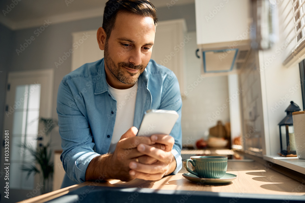 Smiling man texting on cell phone in kitchen. Smiling man texting on cell phone in kitchen.