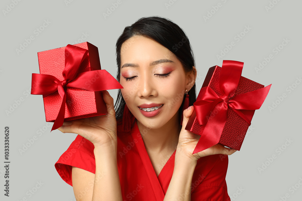 Beautiful young happy Asian woman with gift boxes on grey background. Chinese New Year celebration Beautiful young happy Asian woman with gift boxes on grey background. Chinese New Year celebration