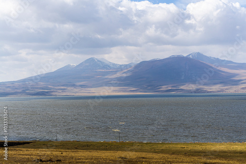 Plowed field on the edge of Lake Paravani. Low waves on the water. Mountains, hills, blue sky with clouds in the background photo