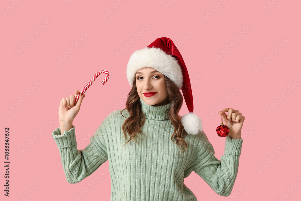 Fototapeta premium Young woman in Santa hat with Christmas ball and candy cane on pink background