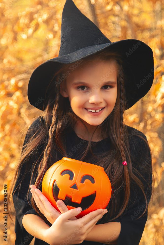 Portrait of a handsome cute girl in a black witch costume asking for candy on Halloween eve. The child celebrates and holds a pumpkin bucket for treats. Portrait of a handsome cute girl in a black witch costume asking for candy on Halloween eve. The child celebrates and holds a pumpkin bucket for treats.