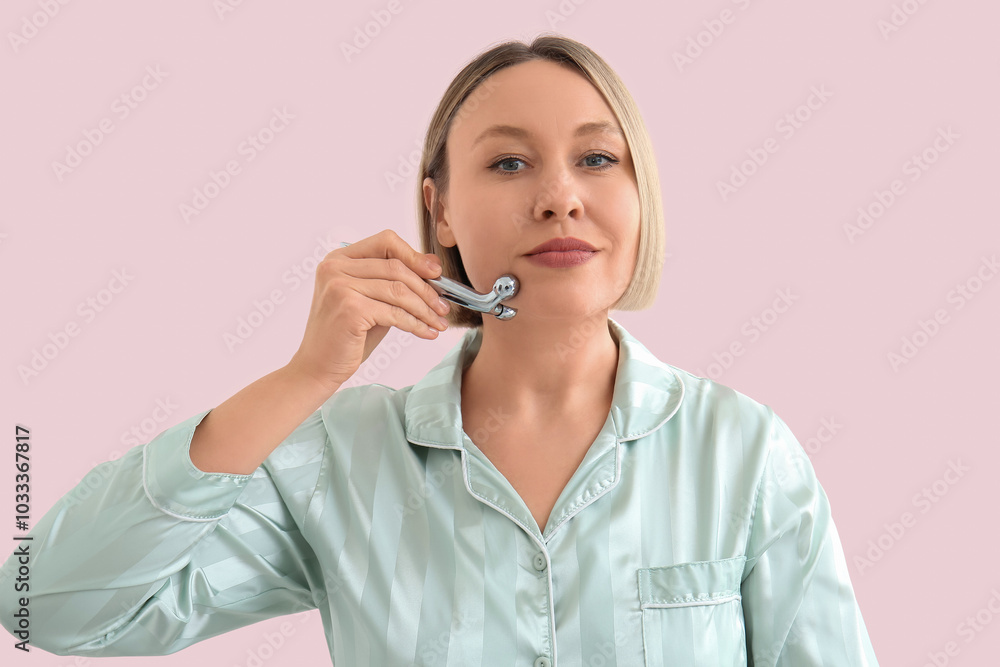 Woman using face massage roller on pink background Woman using face massage roller on pink background