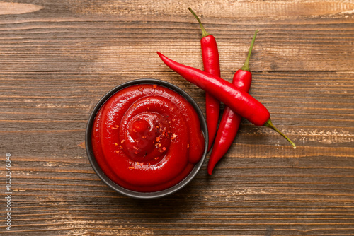 Bowl of chili sauce and fresh peppers on wooden background