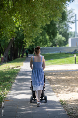 A woman in a blue dress is walking down a sidewalk with a stroller